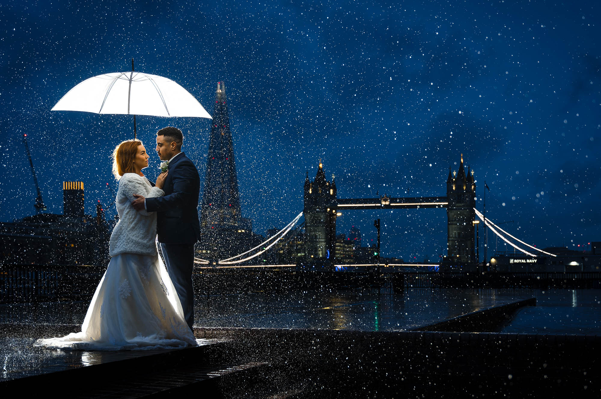 Bride and groom holding a white umbrella in the rain with Tower, Bridge in the background