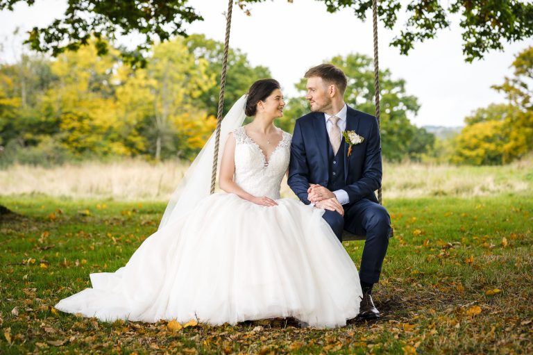 Bride and groom sitting on swing in the meadows at Swllows Oast wedding venue, Ticehurst, East Sussex