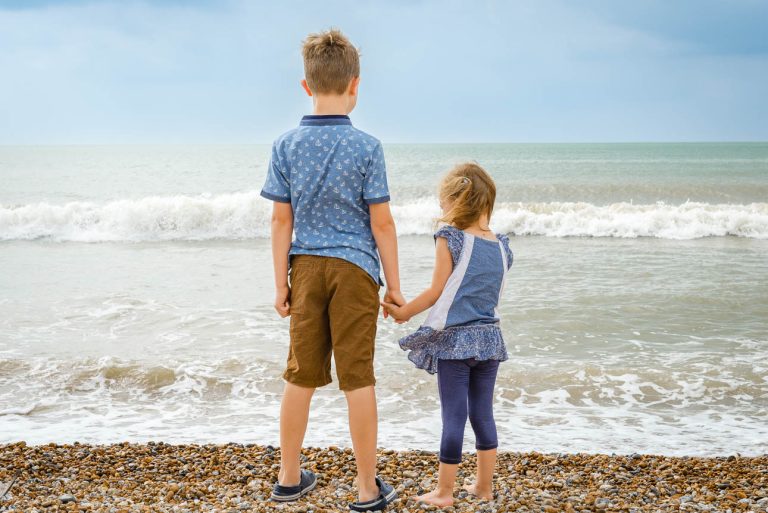 Camber Sands photo shoot, Sussex - brother and sister holding hands on beach and looking out to sea