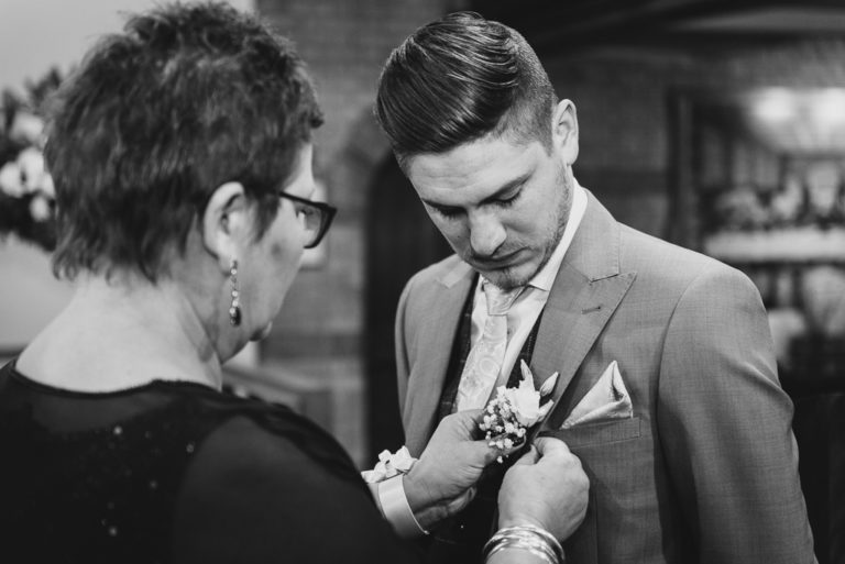 Groom's mother adding button hole to the groom's jacket before the wedding | Sidcup Wedding of Becky & Hugo | Oakhouse Photography