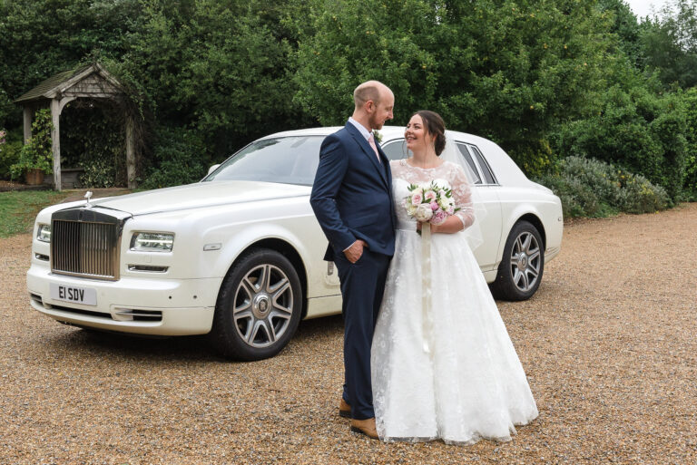 Bride and groom posing in front of their white Rolls Royce wedding car at Swallows Oast, Ticehurst, East Sussex | Oakhouse Photography
