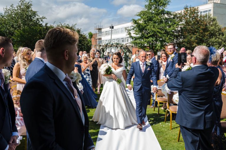 Bride coming down the aisle for outdoor wedding ceremony at Mercure Maidstone Great Danes Hotel wedding