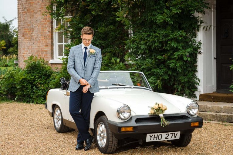 Portrait of groom standing next to a classic MG motor car at Sprivers Mansion wedding venue, Kent