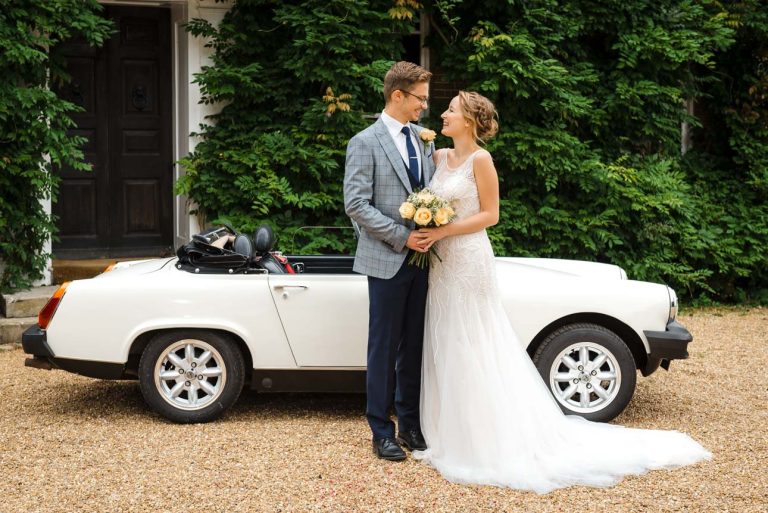 Portrait of bride and groom in front of MG classic car at Sprivers Mansion wedding venue, Kent