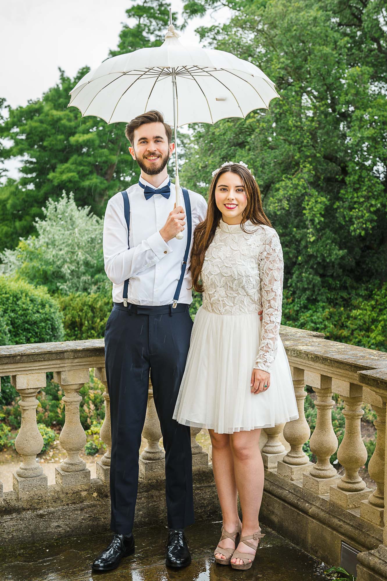 Bride and groom portrait at the top of the steps of Danson House, Danson Park, Bexleyheath, Kent while holding a parasol umbrella in the rain