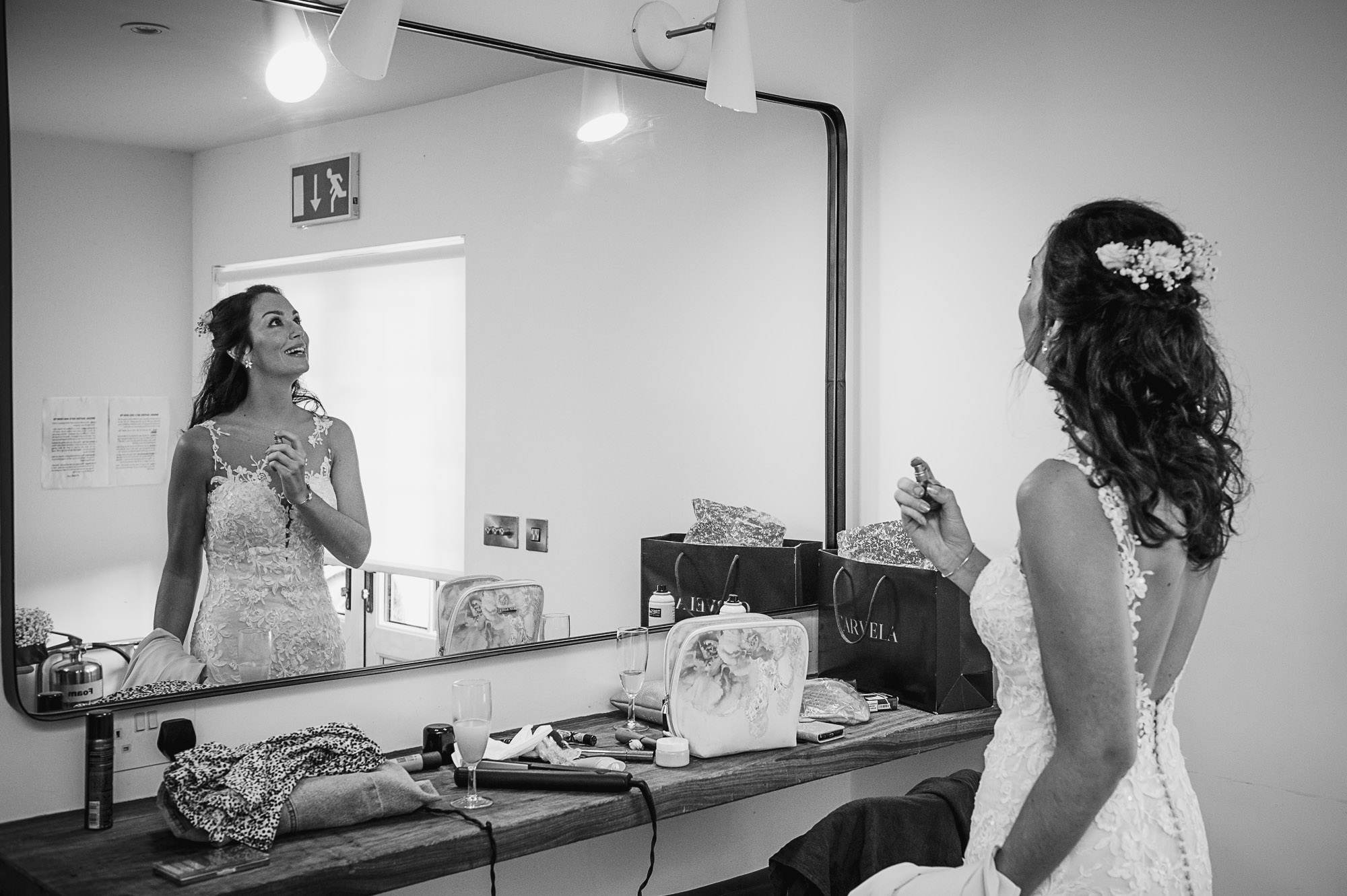 Documentary photograph of bride spaying on perfume with reflection in the mirror in The Bridal Suite suite at Swallows Oast wedding venue in Ticehurst, East Susssex