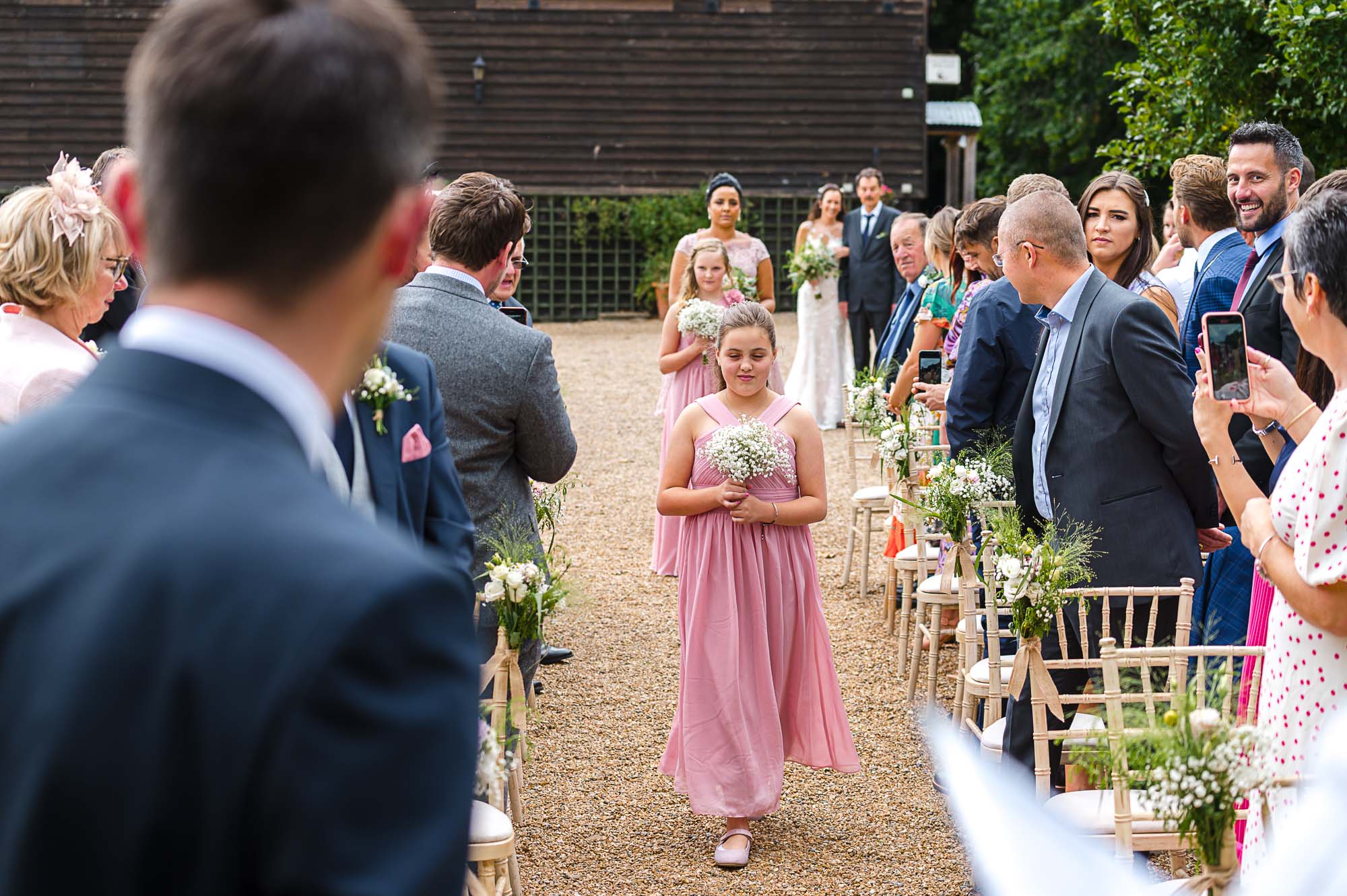 Bridesmaids walking down the aisle with bride and her father in the background for the outdoor wedding ceremony at The Pavilion at Swallows Oast wedding venue in Ticehurst, East Sussex