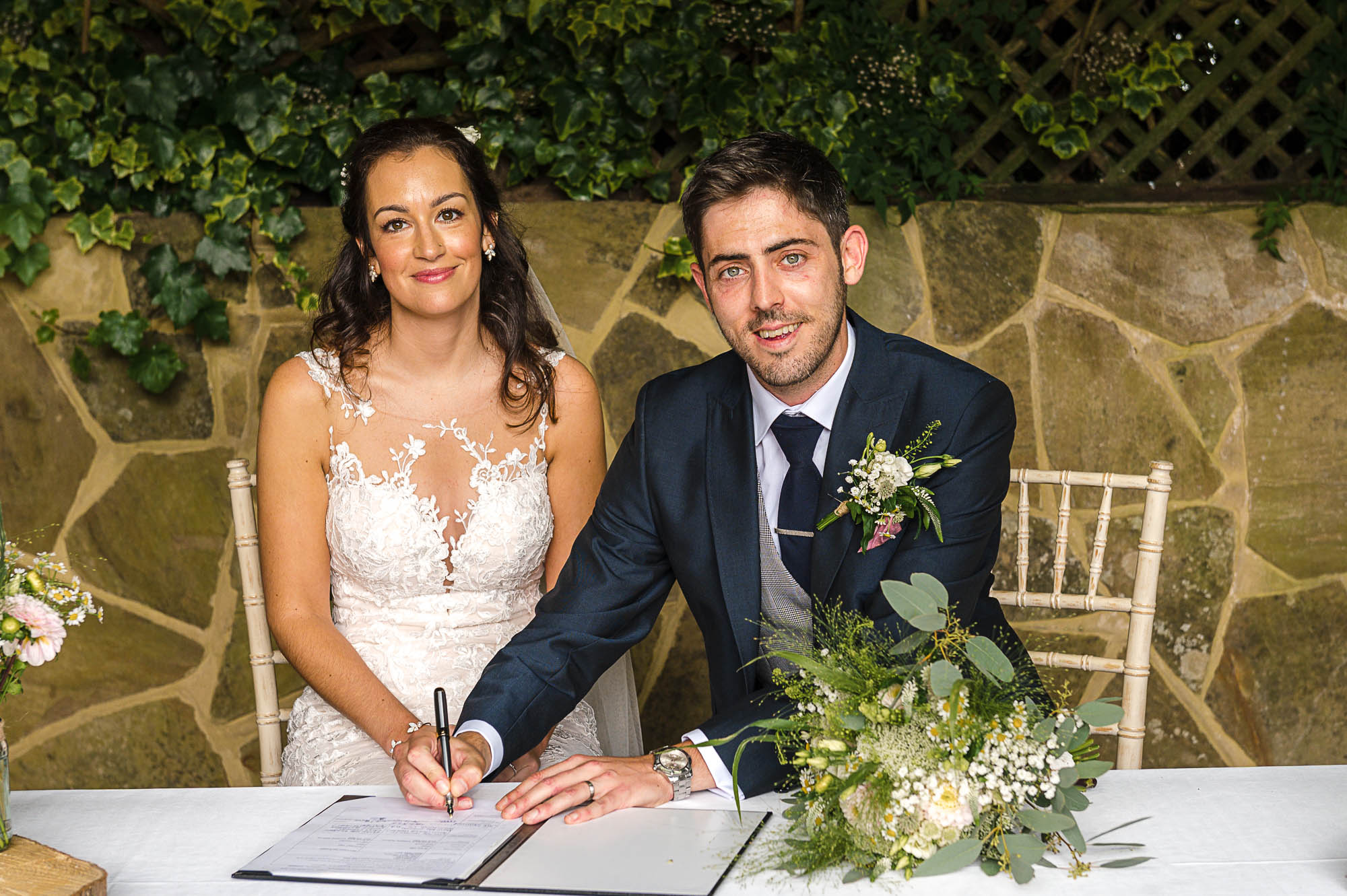 Bride and groom signing their wedding certificate at their outdoor wedding ceremony under The Pavilion at their Swallows Oast wedding venue in Ticehurst, East Sussex