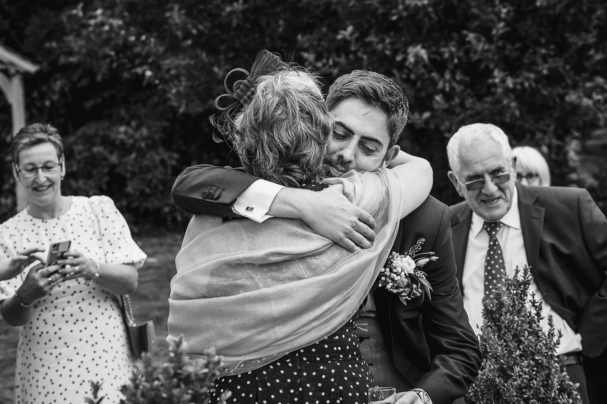 Candid documentary photograph of groom hugging his mother at his Swallows Oast wedding venue in Ticehurst, East Sussex