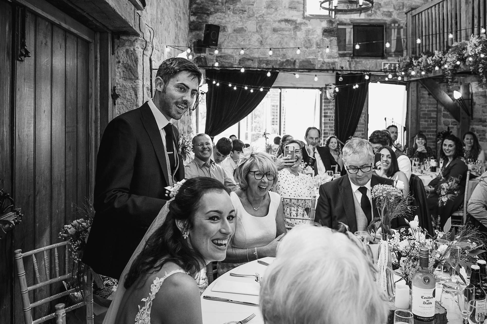 Candid documentary portrait of groom and wedding party during the groom's speech during the reception at Swallows Oast wedding venue, Ticehurst, East Sussex
