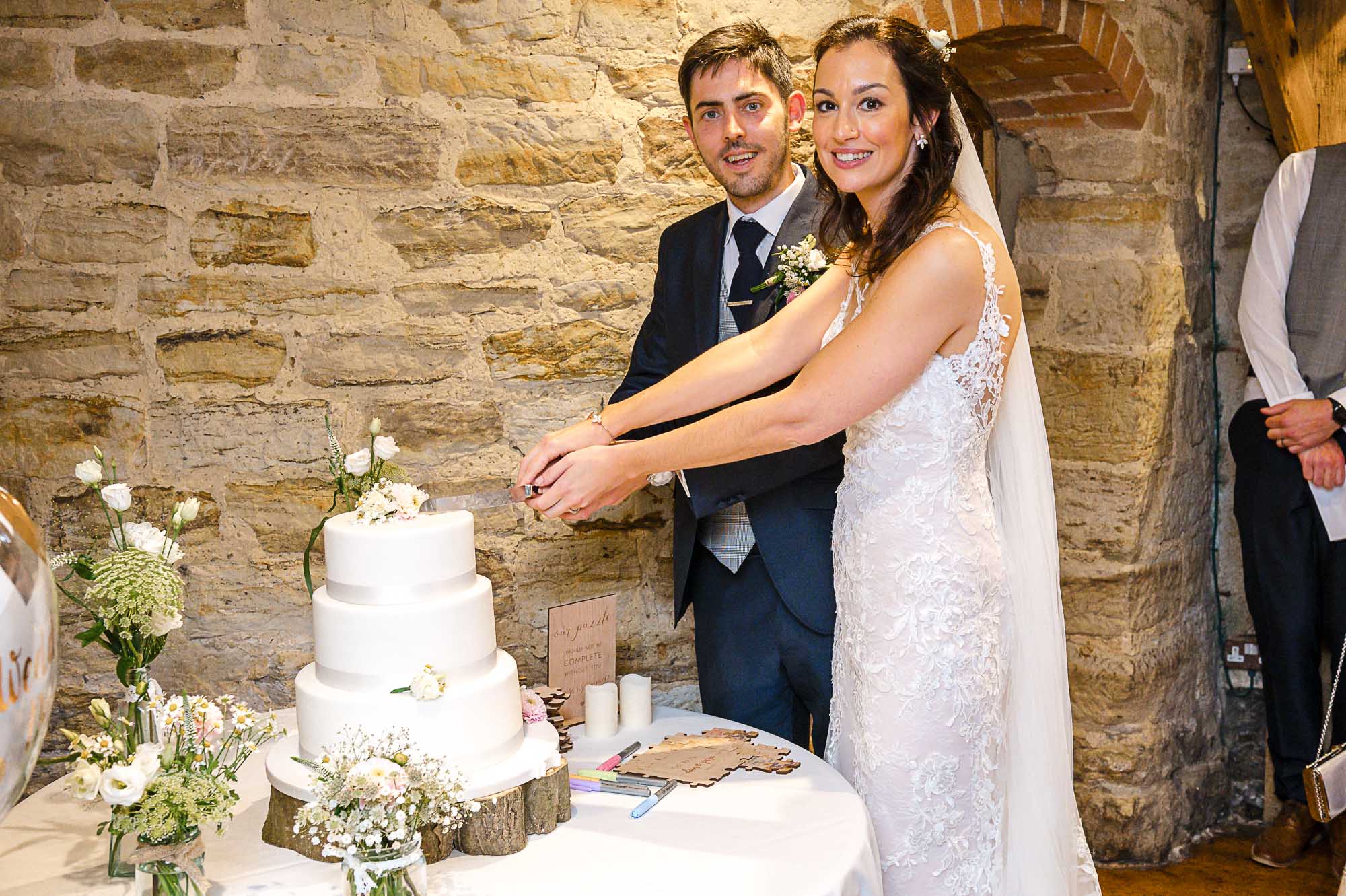 Bride and groom cutting their wedding cake in the barn reception at Swallows Oast wedding venue, Ticehurst, East Sussex