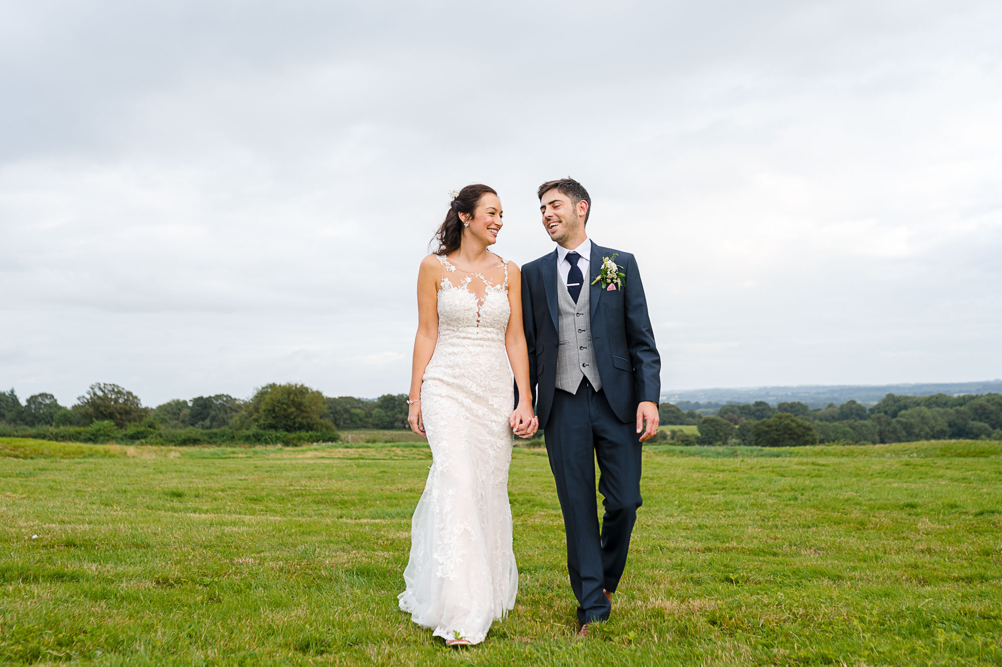 Bride and groom walking hand in hand in Swallows Oast wedding venue's meadow
