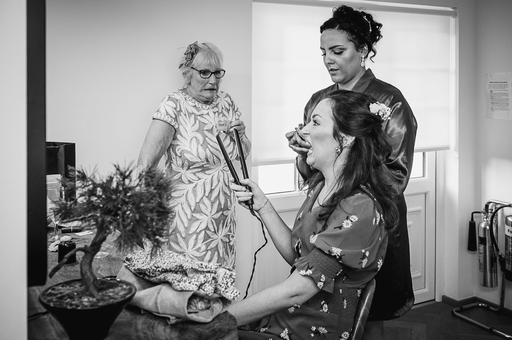 Bridesmaid, maid of honour and bride's mother having fun while her was being hair styled during bridal prep in The Bridal Suite at Swallows Oast wedding venue in Ticehurst, East Sussex