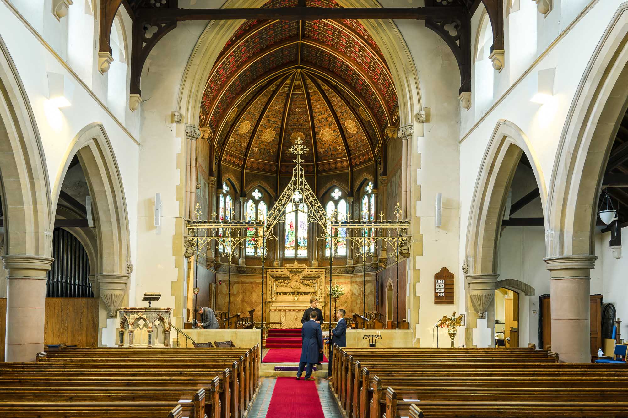 Internal view of St John the Evangelist Church, Bexley with groom and best man speaking to the vicar of the church ahead of the wedding ceremony.